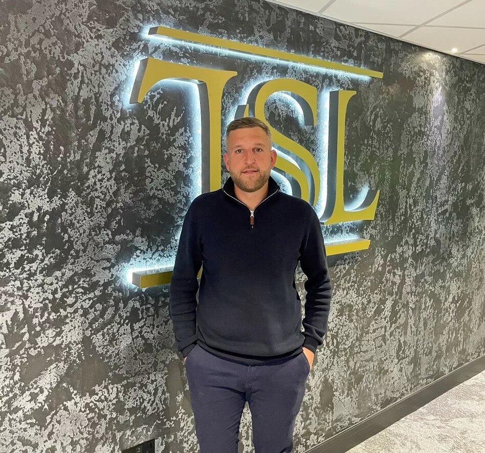 Photo of Antony Knight stood in front of a neon TSL sign.
